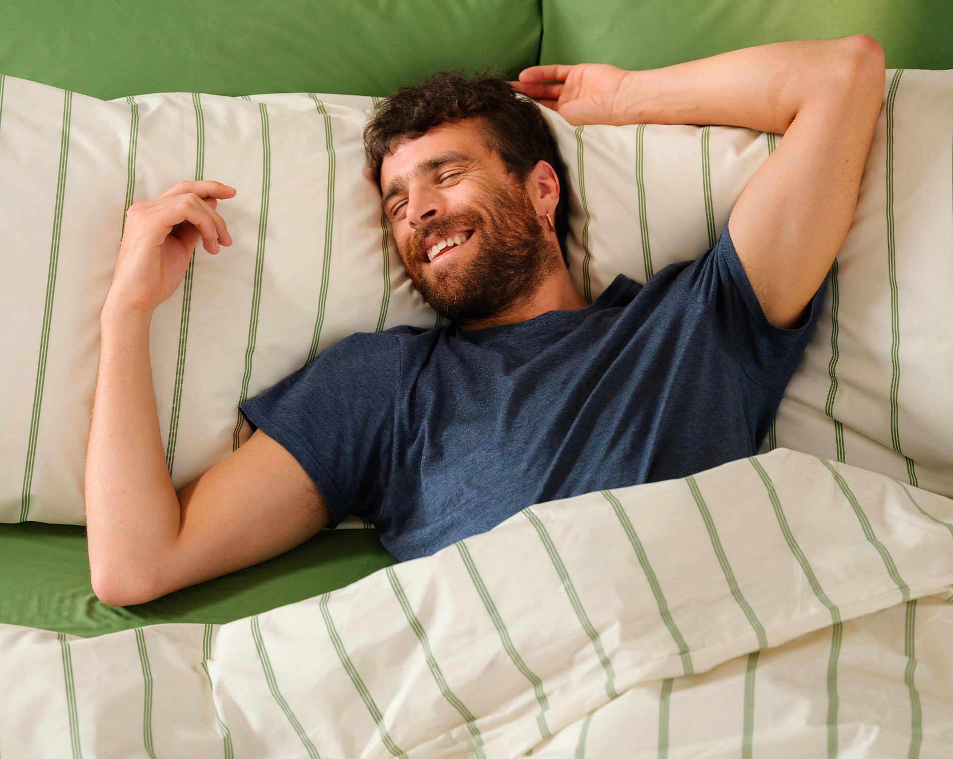 Ragazzo felice sdraiato su letto a righe crema e oliva Dalfilo